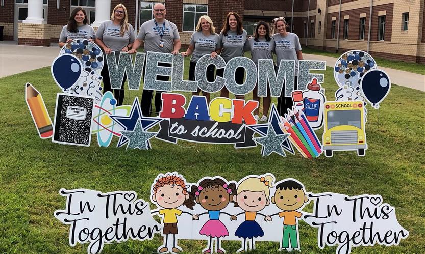 A group takes a photo with a Welcome Back sign